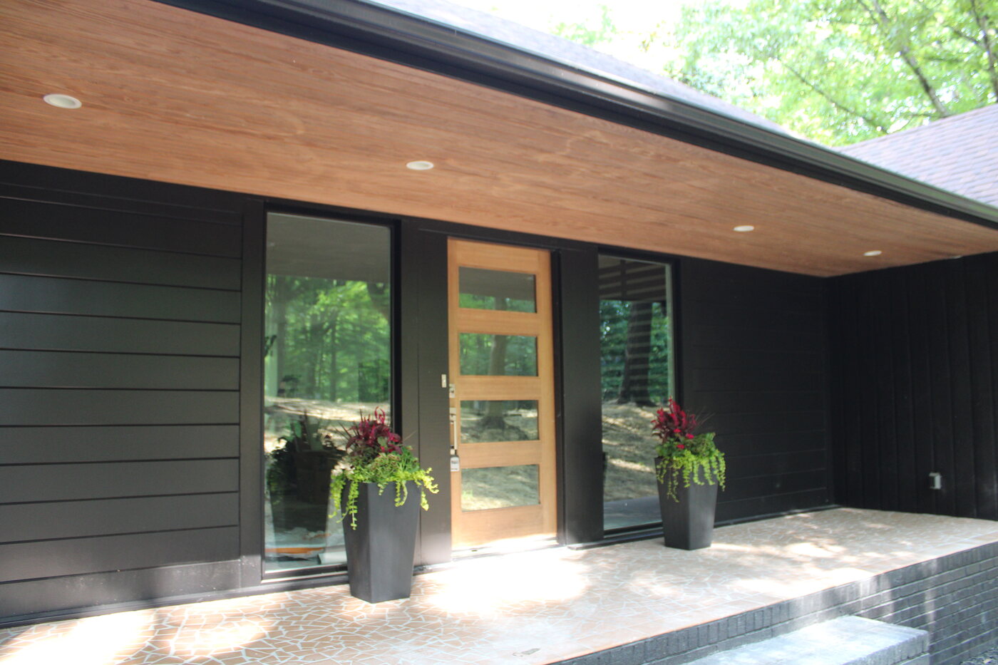 Dramatically renovated home with black exterior and modern wood entry, tucked into the trees